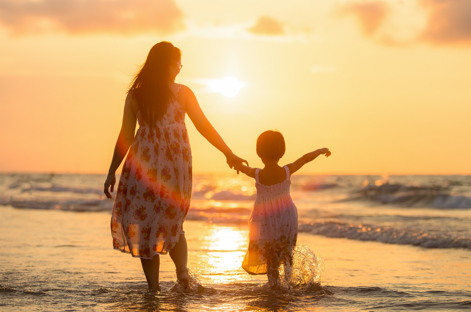 Woman and child walking on the beach at sunset. Golden sunset tones. 